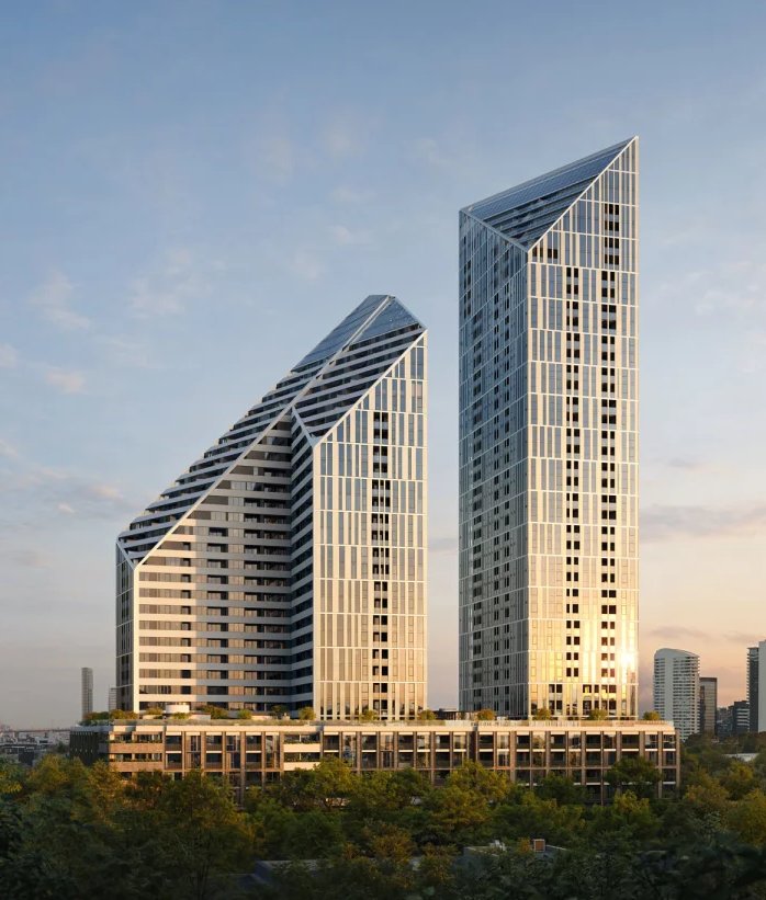 Two faceted residential towers rising above a wooded district at dusk