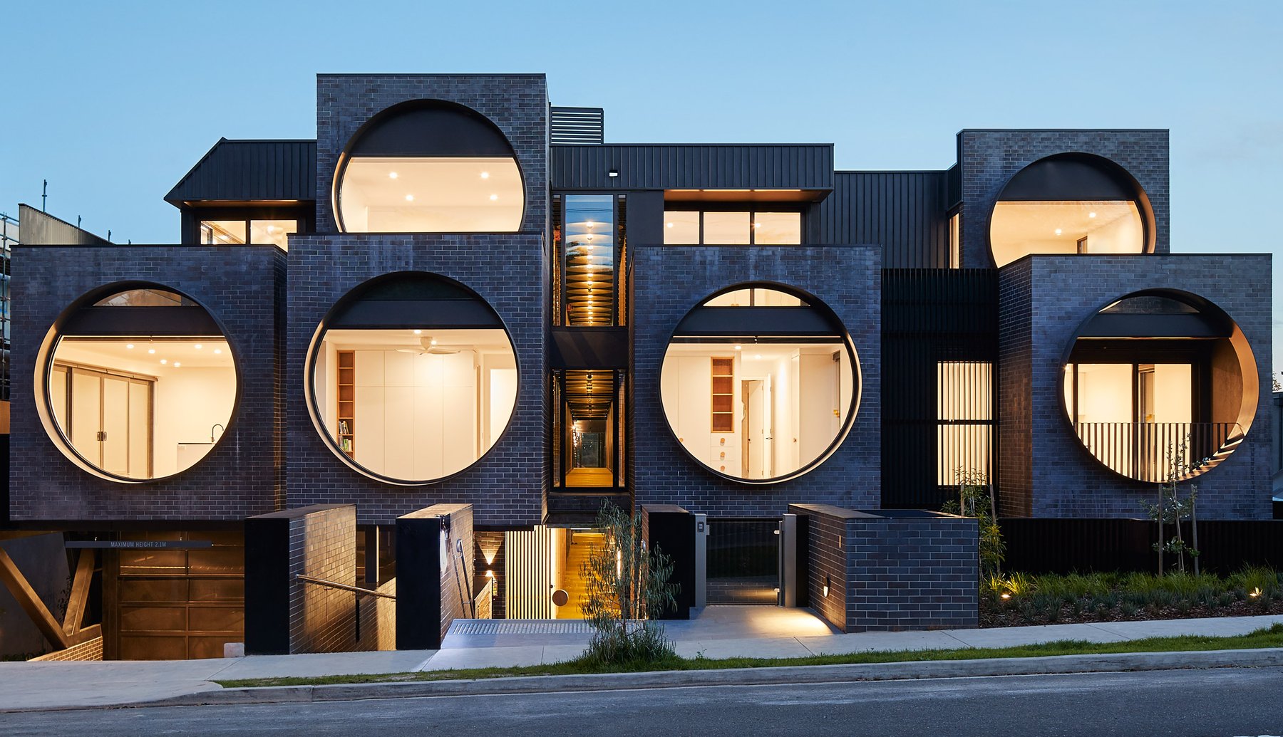 Dark brick apartment building with large circular windows, lit from within at dusk